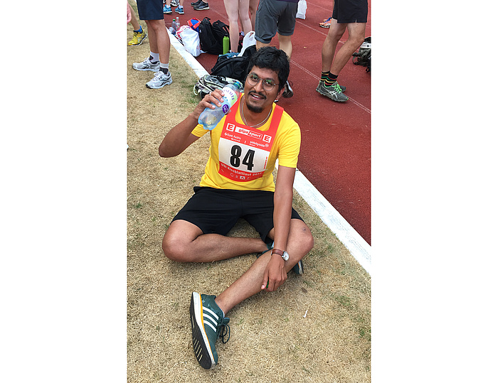 Erschöpfter aber zufriedener Läufer in gelbem Shirt mit der Startnummer 84 hält eine Wasserflasche.