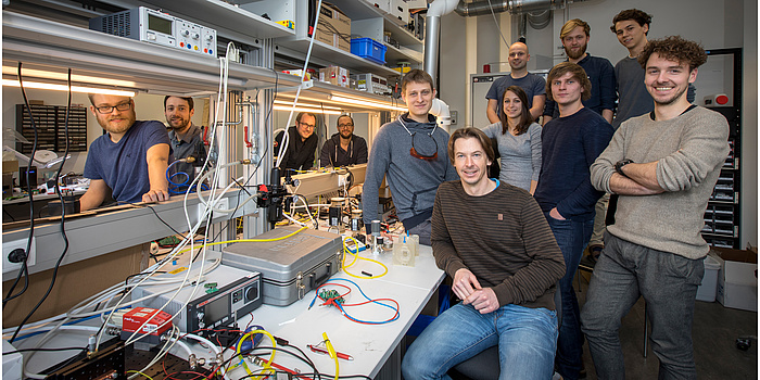 Eine Gruppe von Forschern steht um einen Arbeitstisch in einem bunten und vollgeräumten Labor