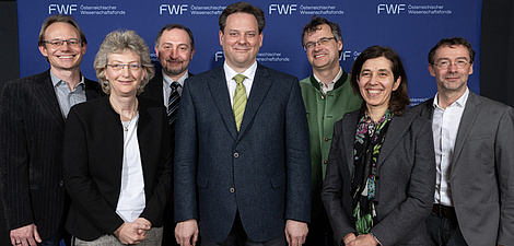 Seven people stand in a row and smile at the camera.