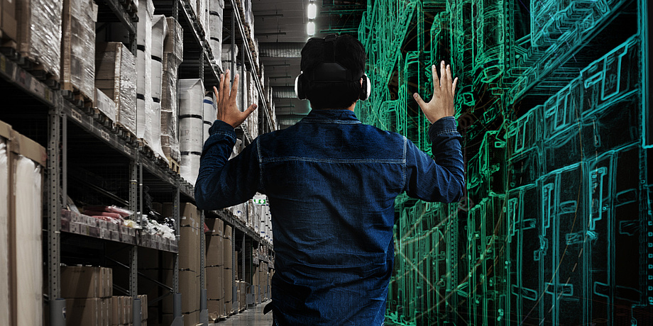 Rear view of a man with VR glasses on his head. To his left is a shelf with numerous boxes, to his right a computer-generated image of a shelf.