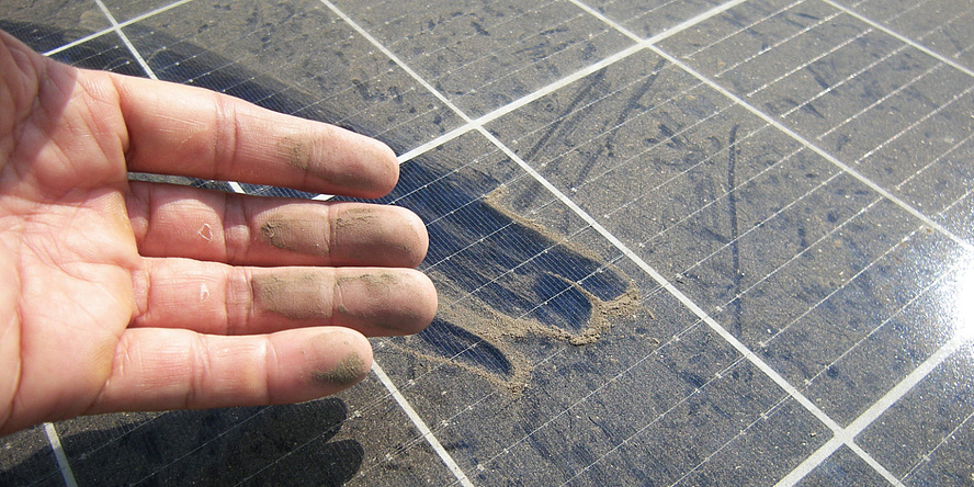 A hand over a photovoltaic system covered in dust.