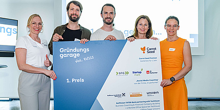 Two men and three women hold a poster with company logos and the inscription Start-up Garage 1st Prize.