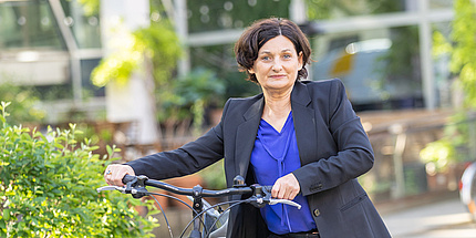 Eine Frau in dunklem Blazer schiebt ein Fahrrad.