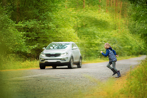 Ein Kind rennt auf eine Straße, auf der ein Auto fährt.