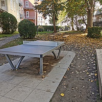 Outdoor Lernort zwischen Mandellstraße 13 und Lessingstraße 25 mit einem Tisch, Bänken und einem Tischtennistisch. 