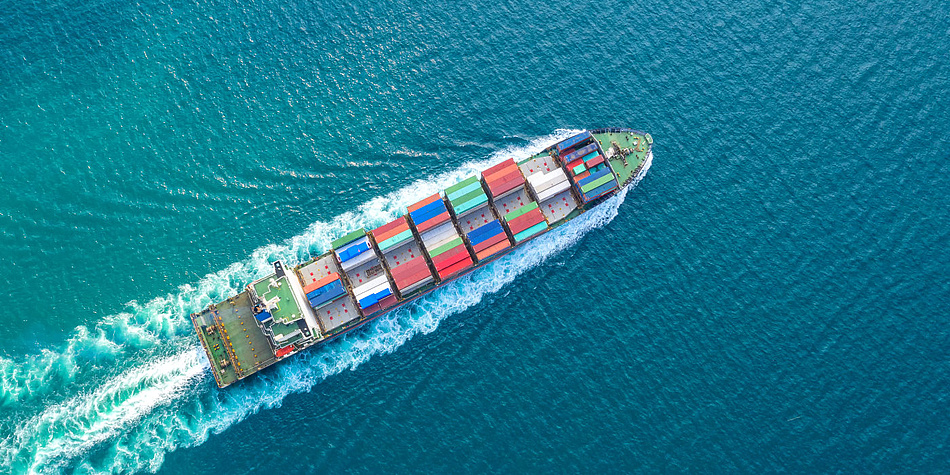 Ein Containerschiff fährt übers Meer, aufgenommen von oben.