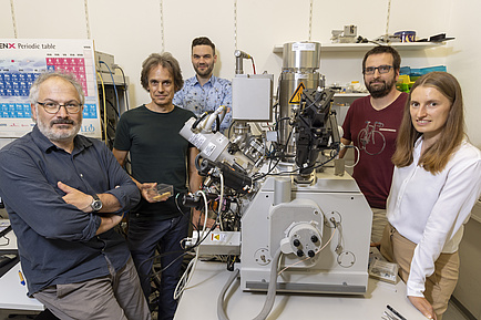 Five people are standing around a table with a microscope on it.