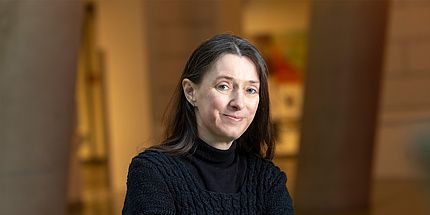 Eine Frau sitzt mit schwarzem Pullover und blickt frontal in die Kamera.
