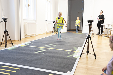 A child is running on a test track and is filmed by two cameras.