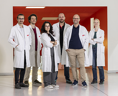 Six people in white lab coats, two women and four men, are smiling into the camera.