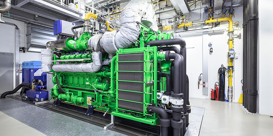 A test stand for large engines in a hall. The frame around the test stand is green, at the top is a large pipe for discharging the exhaust gases.