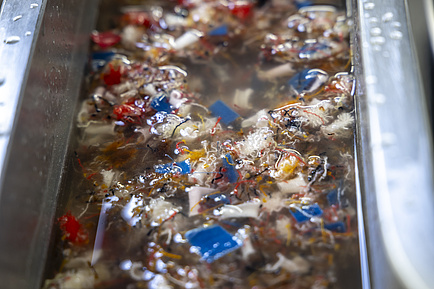 Viele bunte Fetzen schwimmen in einer mit wasser gefüllten Metallrinne.