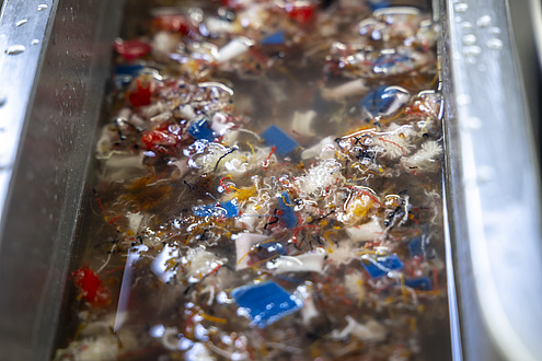 Many colourful shreds are floating in a metal channel filled with water.