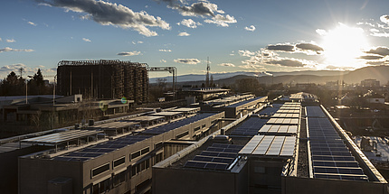 The sun shines on elongated buildings with photovoltaic systems on their roofs.