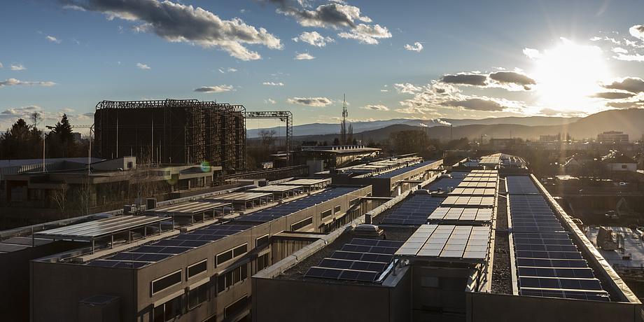 Die Sonne scheint auf langgezogene Gebäude, auf deren Dächer sich Photovoltaik-Anlagen befinden.