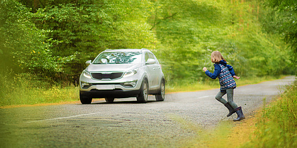 Ein Kind läuft auf eine Straße, auf der ein Auto fährt.