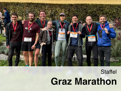 The image shows eight smiling participants from IEE standing in a row after the relay race at the Graz Marathon. They are proudly displaying their medals, which they are wearing around their necks.