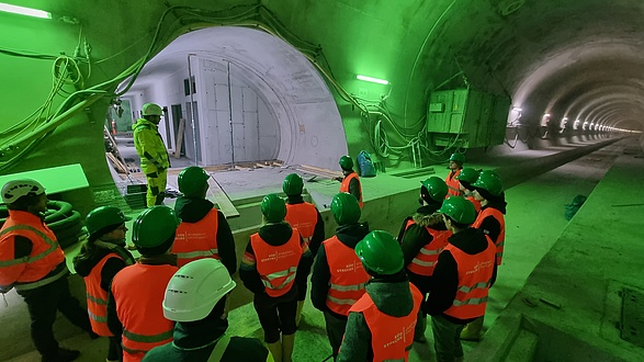 Eine Gruppe von Menschen steht in einer Tunnelröhre, die grün beleuchtet ist.