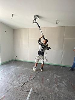 A man holds a large grinding machine to a ceiling. He is wearing an exoskeleton.