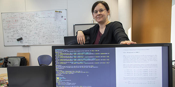 Eine junge Frau steht hinter einem Computerbildschirm und hat eine Hand auf ihn gelegt. Der Computerbildschirm ist blau und voll mit weißer Schrift.