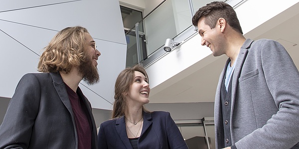 Two young men and a young woman, all wearing jackets, are having a conversation.