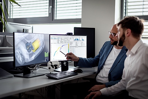 Two men are discussing in front of two screens.