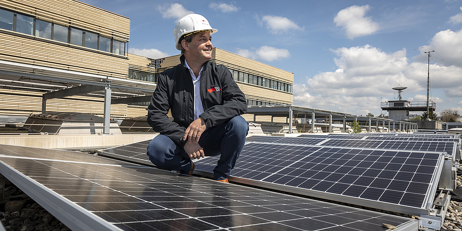 A man wearing a black jacket and a white protective helmet in the midst of solar panels.