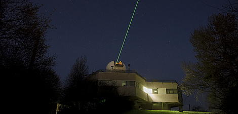 A laser light beam is directed into the night sky from the roof of a building.