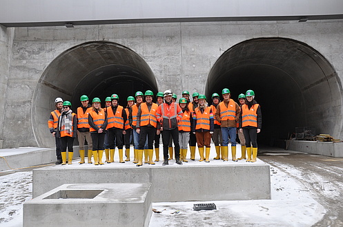 Eine Gruppe von Menschen steht vor zwei Tunnelöffnungen.