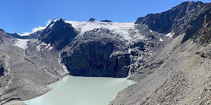 A glacier lies above a steep rock face, under which a meltwater lake can be seen.