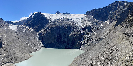 Ein Gletscher liegt oberhalb einer steilen Felswand, unter der ein Schmelzwassersee zu sehen ist.