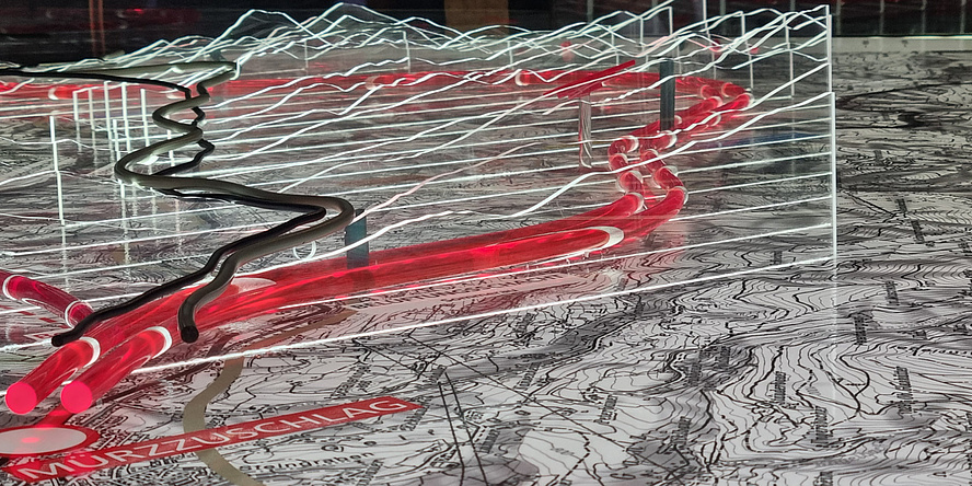 A surface with a map printed on it. Above it are two red plastic tubes that trace the course of a tunnel.