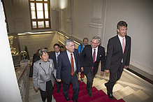 Six people, five men and one woman, walk up the stairs of the Alte TEchnik. The floor is covered with a red carpet.