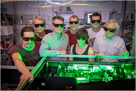 Eine Forschenden-Gruppe im Physik-Labor in grünes Licht getaucht