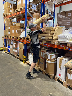 A man lifts a large parcel onto a shelf. He is wearing an exoskeleton.