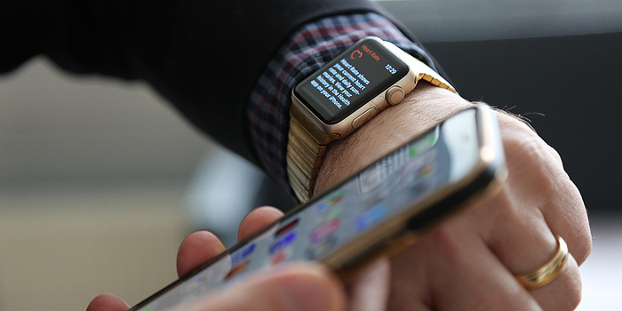 Two hands. One hand holds a Smartphone, the other a Smartwatch.