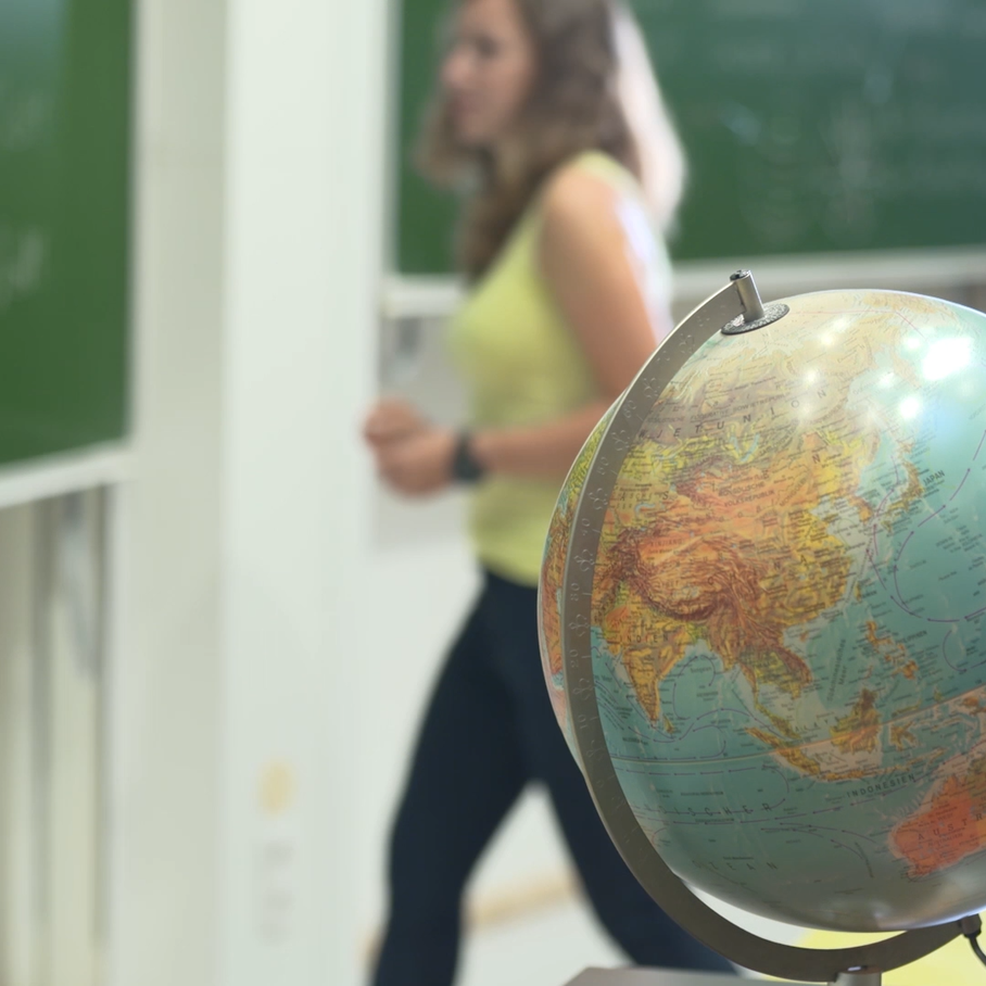 Woman at a blackboard behind a globe.