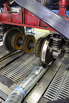 A picture of a train axle. The train tyre is standing on a track and in front of it is a pipe for measuring emissions.