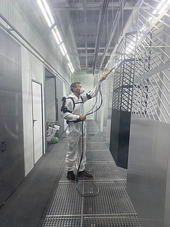 A man in a white overall wears an exoskeleton and sprays a grid with a nozzle.