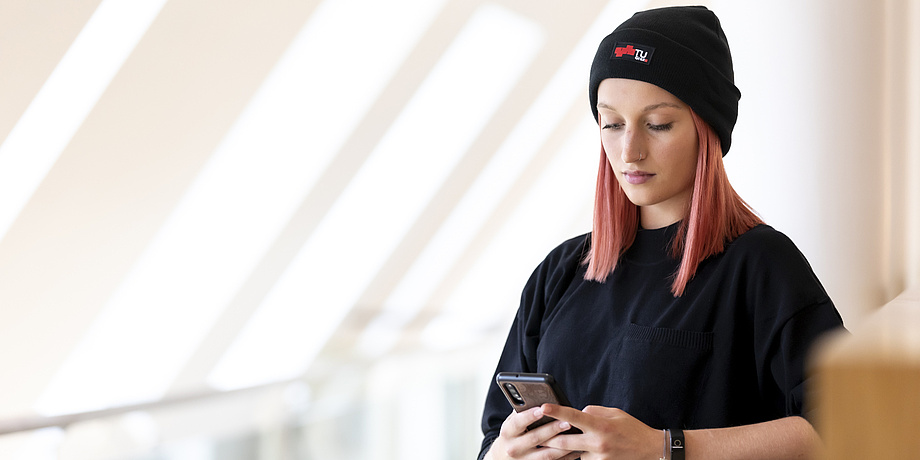 A woman wearing a black cap and a black T-shirt is looking intently at a smartphone.