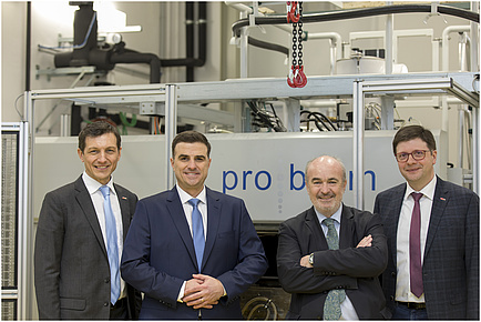 Vier Herren stehen lächelnd vor einer Maschine.